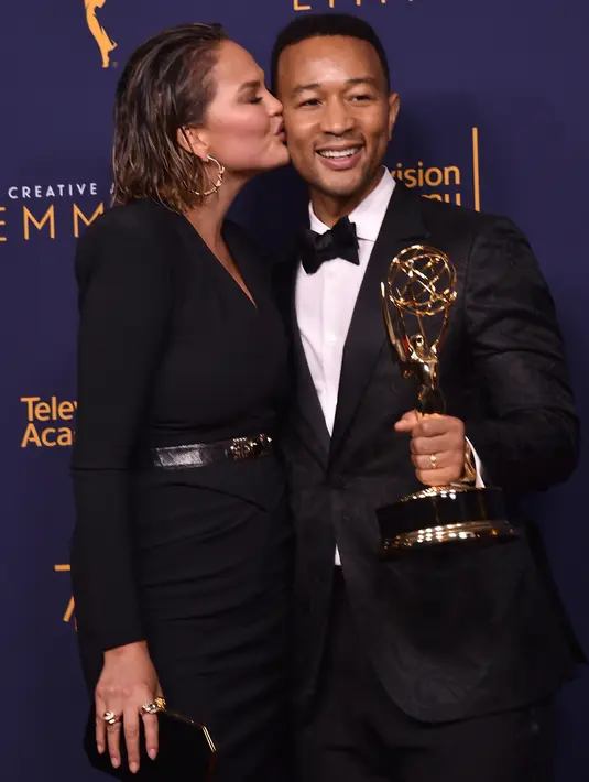 Chrissy Teigen mencium John Legend selama Creative Arts Emmy 2018 di Microsoft Theater di Los Angeles, California, AS (9/9). Penghargaan ini untuk artis yang telah memenangkan di Emmy, Grammy, Oscar, dan Tonys. (AFP Photo/Alberto E. Rodriguez)