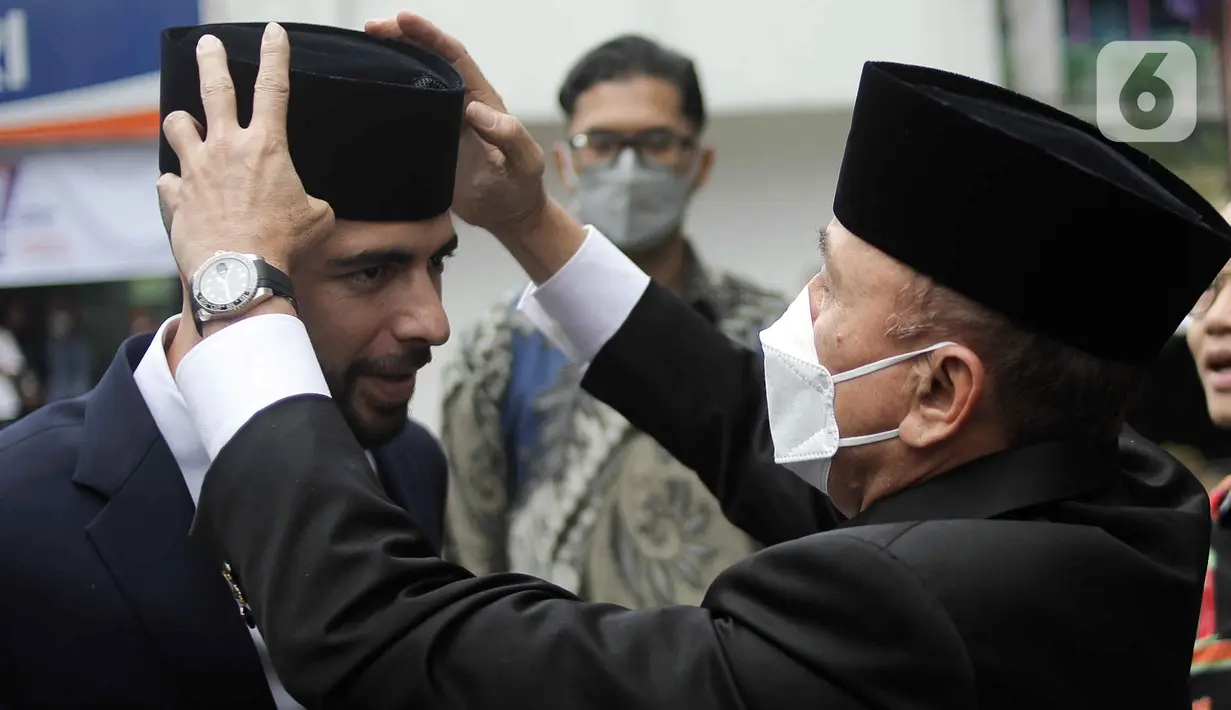 Ketua Umum PSSI Muhammad Iriawan (kanan) memegang peci pemain sepak bola Jordi Amat usai menjalani Sumpah Janji Setia Pewarganegaraan di Kantor Wilayah Kementerian Hukum dan HAM DKI Jakarta, Kamis (17/11/2022). Jordi Amat resmi menjadi Warga Negara Indonesia (WNI) setelah prosesi pengambilan sumpah yang digelar secara tertutup. (Liputan6.com/Herman Zakharia)
