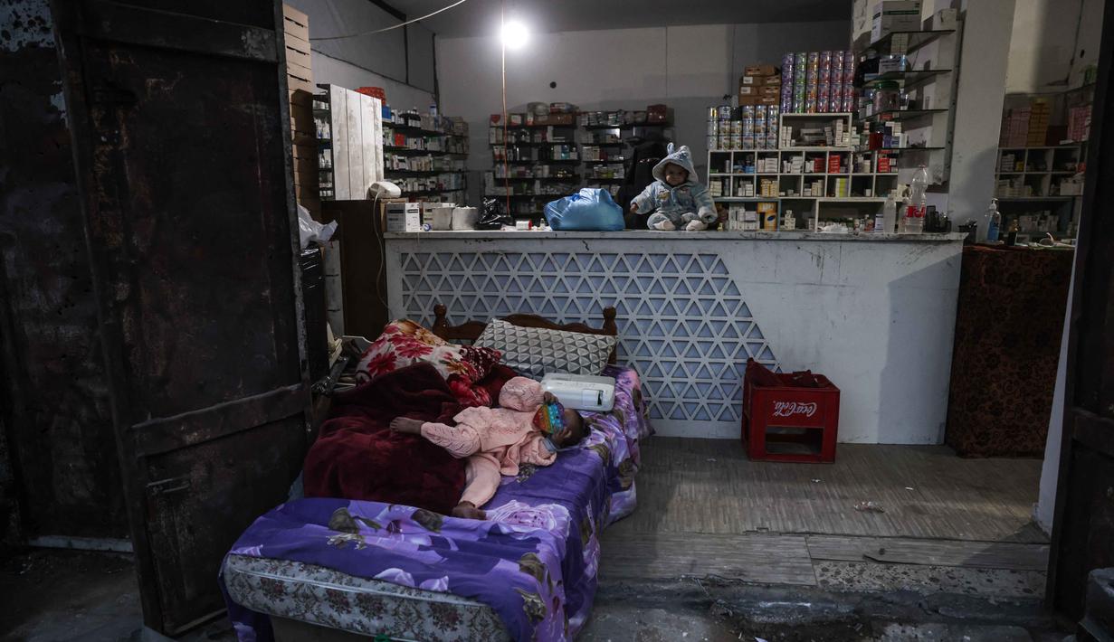 Di sana, mereka harus berjuang untuk mendapatkan akses terhadap kebutuhan dasar seperti air dan makanan. Tampak dalam foto, seorang bayi duduk di atas meja kasir di sebuah apotek di lingkungan Al-Saftawi, sebelah barat kota Jabalia di Jalur Gaza utara pada Rabu 10 Desember 2025. (BASHAR TALEB/AFP)