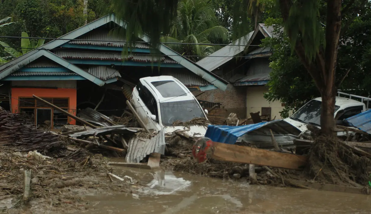 Kendaraan hanyut oleh banjir bandang di sebelah rumah-rumah di desa Radda di Kabupaten Luwu Utara, Sulawesi Selatan (14/7/2020). Hujan lebat yang mengakibatkan tiga sungai meluap telah menyapu rumah-rumah, kendaraan dan berbagai fasilitas umum di enam kecamatan di Kabupaten Luwu Utara. (AFP/Aryanto)