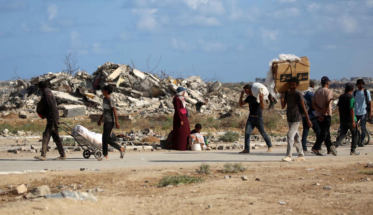 Otoritas Gaza menyeru kepada dunia internasional untuk menekan Israel agar menghentikan agresi serta membuka jalur bantuan tanpa hambatan. Tampak dalam foto, warga Palestina, membawa tas dan kardus kosong, berjalan melewati bangunan yang hancur saat mereka kembali dari titik distribusi makanan yang dikelola oleh Yayasan Kemanusiaan Gaza (GHF) yang didukung AS dan Israel, di dekat koridor Netsarim di Jalur Gaza tengah pada 5 Oktober 2025. (Eyad BABA/AFP)