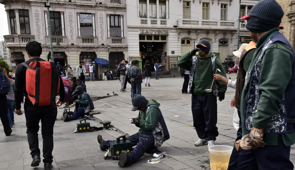 Para tukang semir sepatu bertopeng menunggu pelanggan di kawasan La Paz, Bolivia (29/11). Karena diantara mereka masih ada yang menjalani pendidikan di sekolah dan universitas para tukang semir ini menutup wajahnya. (AFP PHOTO/Aizar Raldes)