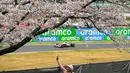 Seorang penonton mendokumentasikan foto melalui gawainya saat seorang pembalap F1 melewati pohon sakura saat melakukan latihan bebas kedua (FP2) F1 GP Jepang 2024 di Sirkuit Suzuka, Jepang, Jumat (05/04/2024). (AFP/Yuichi Yamazaki)