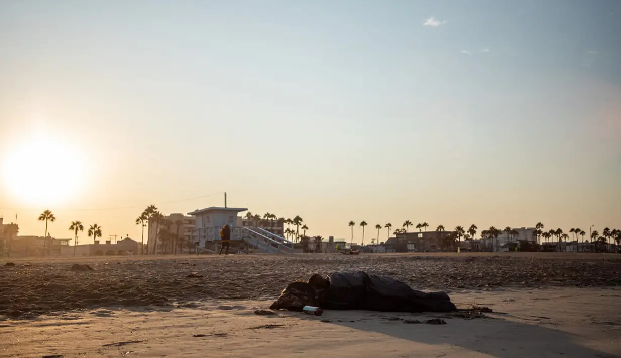 Seorang pria tunawisma tidur pada pagi hari di sebuah pantai di Venesia, California, Amerika Serikat, 12 Agustus 2021. (Apu GOMES/AFP)