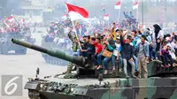 Warga membawa bendera merah putih saat menaiki tank TNI menyaksikan HUT TNI ke-70 di Dermaga Indah Kiat, Cilegon, Banten, Senin (5/10/2015). HUT TNI Ke-70 ditandai atraksi tempur tiga matra TNI Angkata Darat, Laut dan Udara. (Liputan6.com/Faisal Fanani)