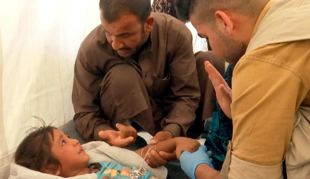 Seorang pria menghibur putrinya saat menerima perawatan dari dokter akibat keracunan makanan di Sebuah tenda medis di kamp Hassan Sham U2, Irak (13/6). Ratusan pengungsi keracunan makanan usai menyantap makanan buka puasa. (AP Photo/Balint Szlanko)