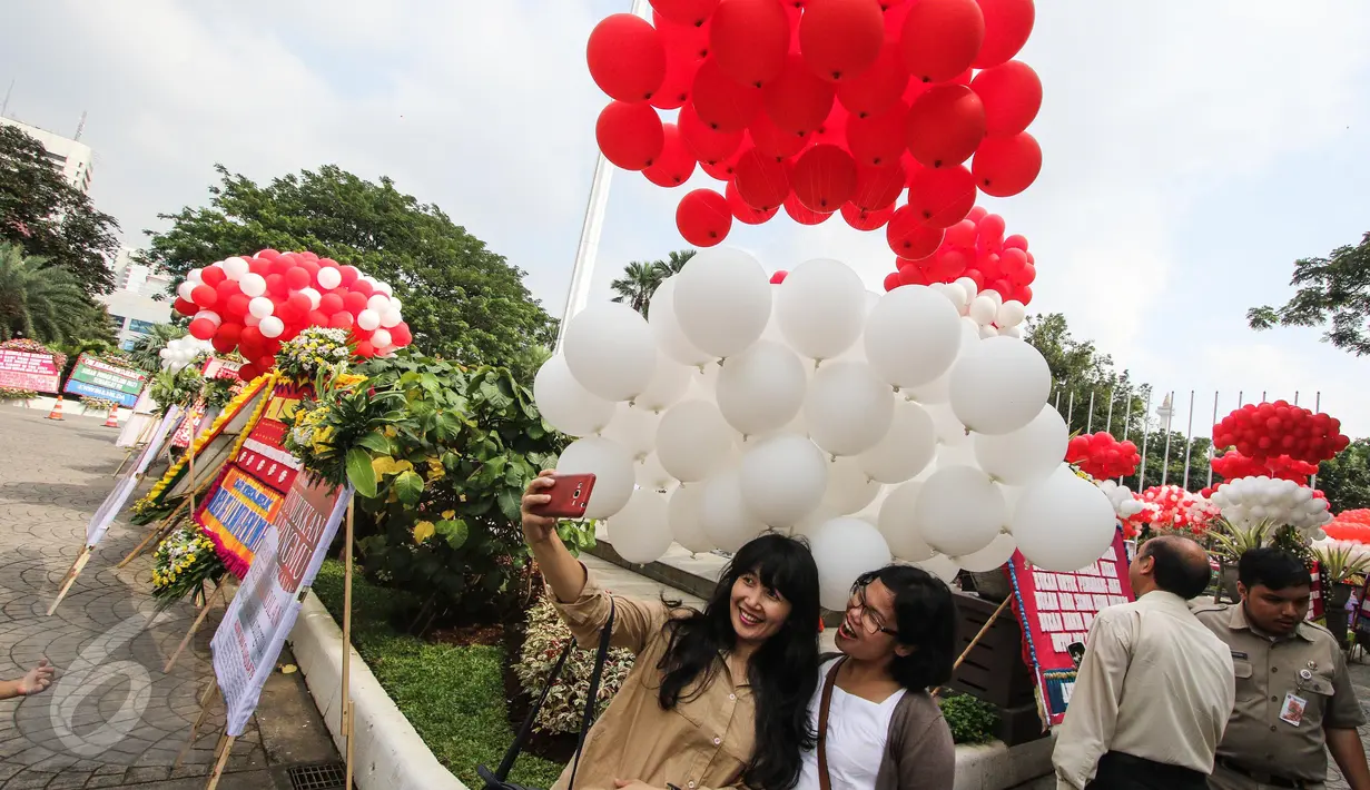Ekspresi warga yang berfoto dengan latar belakang balon berwarna merah putih yang menghiasi halaman Balai Kota, Jakarta, Senin (8/5). Ribuan balon yang berwarna merah putih ini meramaikan kemeriahan di Balai Kota. (Liputan6.com/Faizal Fanani)