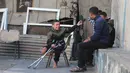 Ibu dan saudara laki-lakinya tewas dalam peristiwa pemboman tersebut. Sementara, salah satu kaki Rateb Mahmoud Qaliq terluka parah dan kemudian terpaksa harus diamputasi. Tampak dalam foto, Rateb Mahmoud Qaliq (kiri) berbincang dengan rekannya di halaman sekolah UNRWA yang telah menjadi tempat penampungan bagi pengungsi Palestina di Deir al-Balah, di Jalur Gaza tengah, pada 3 Desember 2025. (Bashar Taleb/AFP)
