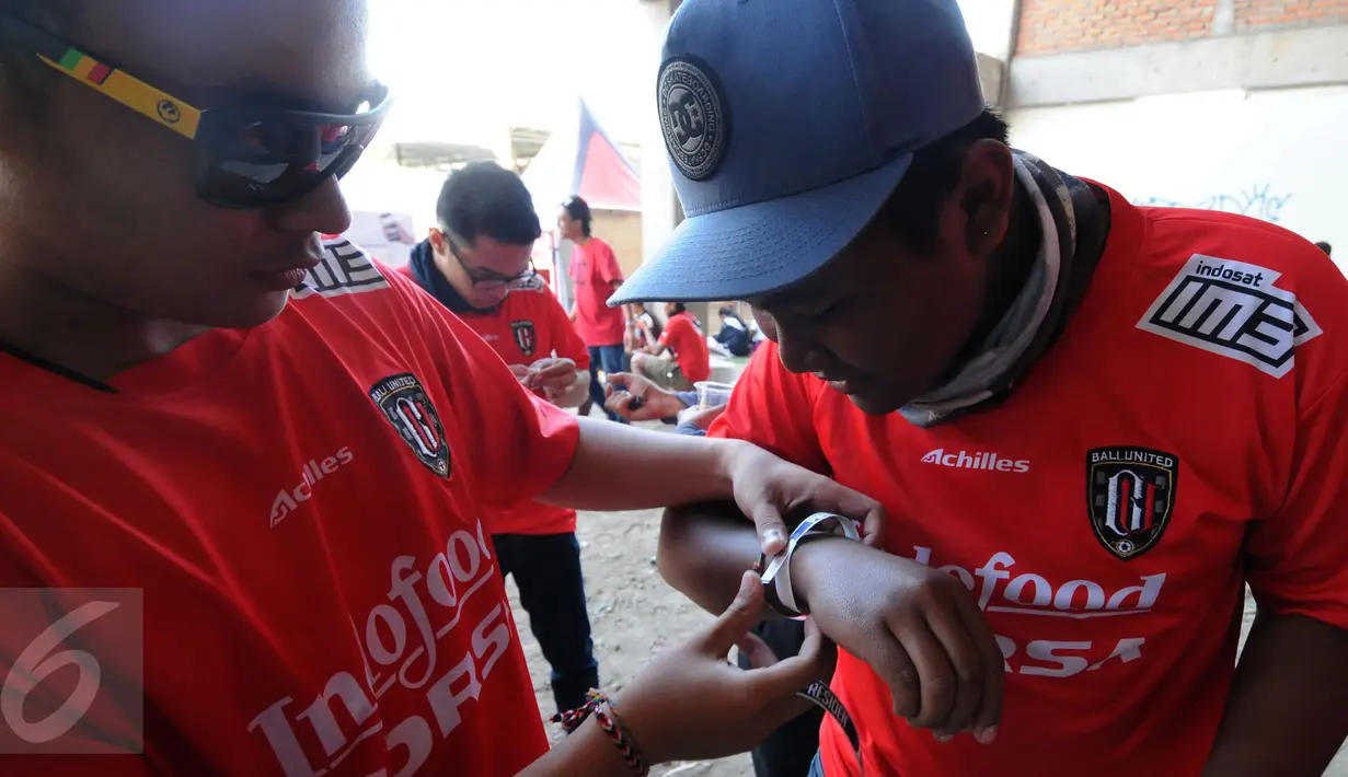 Salah satu suporter membantu memasangkan gelang tiket masuk Stadion I Wayan Dipta, Gianyar, Bali, Minggu (30/8/2015). Jelang pembukaan turnamen Piala Presiden 2015, ribuan suporter menyerbu stadion Dipta, Gianyar, Bali. (Liputan6.com/Helmi Fithriansyah) 