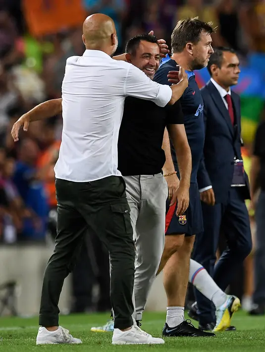 Manajer Manchester City, Pep Guardiola (kiri) memeluk pelatih Barcelona Xavi Hernandez pada akhir sebuah laga amal di Stadion Camp Nou, Kamis (25/8/2022) dinihari WIB. Pertandingan ini menjadi pertemuan perdana Pep Guardiola dan Xavi Hernandez yang pernah bekerja sama di Barcelona sebagai pelatih dan pemain selama rentang waktu 2008–2012. (Josep LAGO / AFP)