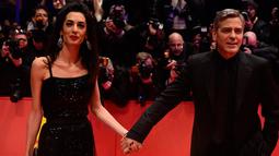 Aktor AS, George Clooney menggandeng mesra istrinya, Amal Alamuddin, saat tiba di karpet merah pemutaran film "Hail, Caesar!" pada pembukaan Berlin International Film Festival ke-66 di Berlin, Jerman, Kamis (11/2). (John MACDOUGALL/AFP)