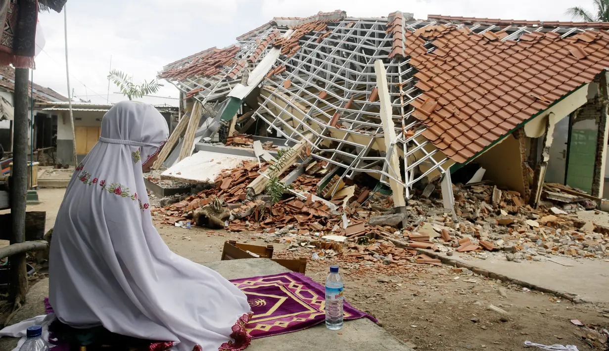 Seorang wanita berdoa di depan puing-puing bangunan di Lombok Barat, Nusa Tenggara Barat (NTB), Sabtu (11/8). BNPB menyatakan gempa Lombok hingga saat ini telah menewaskan 387 orang. (AP Photo/ Firdia Lisnawati)