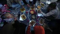 Di beberapa titik di kota Gaza, warga berkumpul bersama keluarga menggelar makanan sederhana untuk berbuka puasa bersama, seperti roti, kurma, dan air minum di lokasi yang dulunya merupakan rumah atau bangunan tempat mereka beraktivitas. Tampak dalam foto, anggota keluarga Al-Najar berbuka puasa selama bulan suci Ramadan di tengah reruntuhan bangunan yang hancur di Kota Gaza, Jumat 13 Maret 2026. (AP Photo/Jehad Alshrafi)