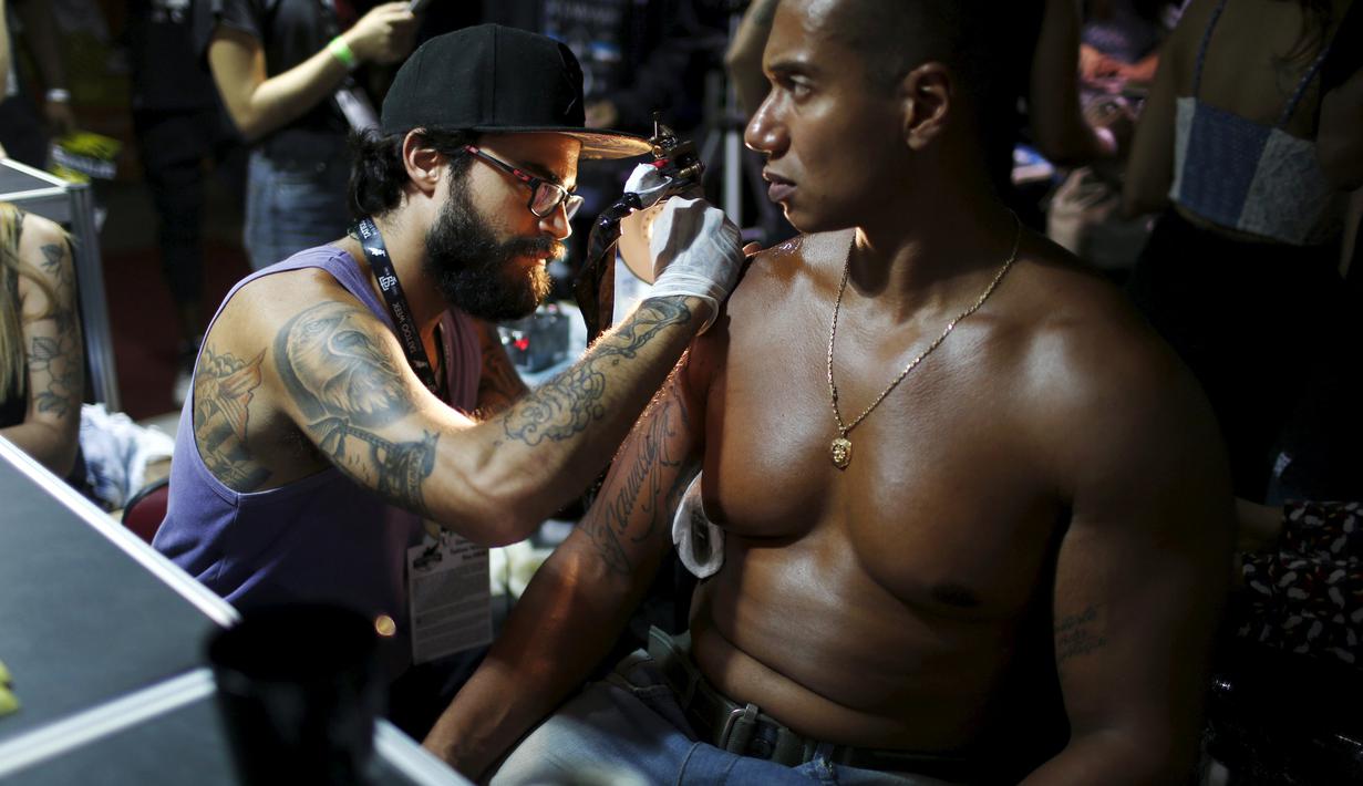 Seorang seniman saat menato seorang pria dibagian bahunya saat Festival Internasional Tattoo Week Rio 2016 ketiga di Rio de Janeiro, Brasil, (22/1/2016). (REUTERS/Pilar Olivares)