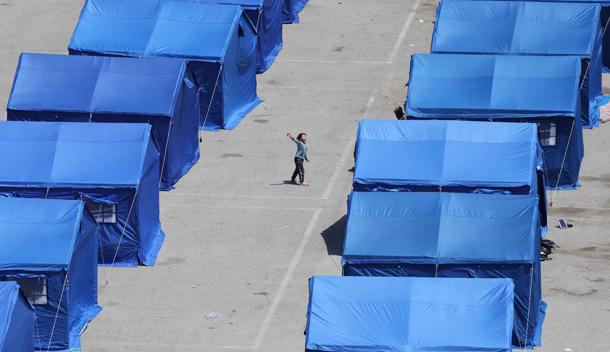 Seorang gadis Lebanon yang mengungsi bermain di antara tenda-tenda biru yang didirikan pemerintah untuk orang-orang yang meninggalkan rumah dan desa mereka di pinggiran selatan Beirut dan Lebanon Selatan, Jumat 22 Mei 2026. (Anwar AMRO/AFP)