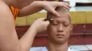 Biksu mencukur alis Ekkapol Chantawong, pelatih tim sepak bola yang diselamatkan dari gua di Thailand pada upacara pentahbisan di Kuil Wat Phra That Doi Wao, Chiang Rai, Selasa (24/7). (Panumas Sanguanwong/THAI NEWS PIX/AFP)