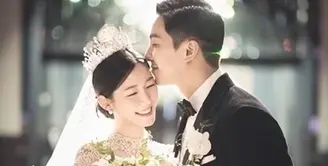 Mengenakan gaun pengantin yang elegan dan tiara mewah, Lee Da In memegang karangan bunga dan tersenyum cerah, sementara suaminya Lee Seung Gi, mengenakan tuksedo di sampingnya, berpose dengan tangan di sakunya dan mencium keningnya. [Foto: IG/byhumanmade]