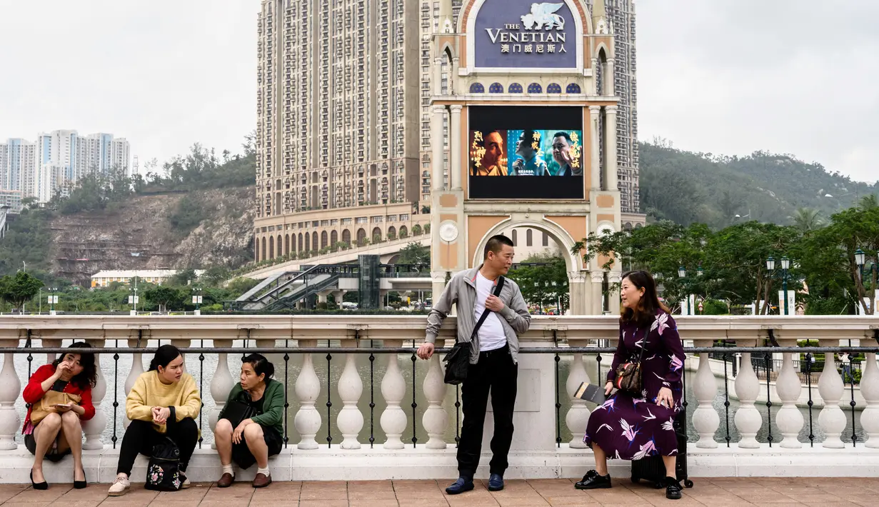 Wisatawan bersantai di sebuah jembatan dengan latar belakang resor kasino The Venetian di Macau, 5 Maret 2019. Macau masuk dalam daerah administrasi khusus di daratan China. (Anthony Wallace/AFP)