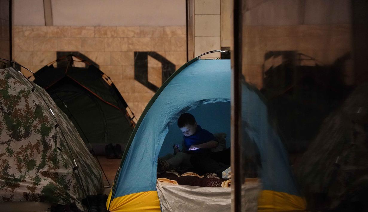 Seorang anak laki-laki duduk di dalam tenda saat orang-orang berlindung di stasiun metro selama serangan udara Rusia, di Kyiv, pada Selasa 3 Februari 2026 pagi waktu setempat. Stasiun Metro Kyiv masih menjadi lokasi perlindungan utama bagi ribuan warga di tengah serangan udara Rusia yang terus meningkat. (Serhii Okunev/AFP)