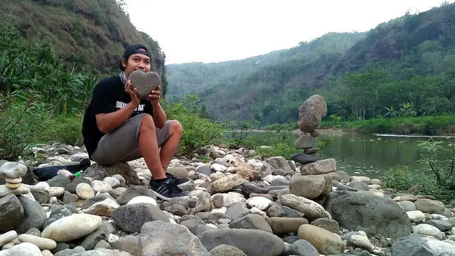 Suryadi sedang mencari batu untuk karya batu bertumpuk
