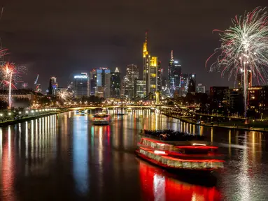 Kapal pesta berlayar mengarungi Sungai Main saat beberapa kembang api meledak dekat gedung-gedung di Frankfurt, Jerman, Sabtu (1/1/2022). Karena pandemi COVID-19, pesta kembang api tidak diperbolehkan. (Photo/Michael Probst)