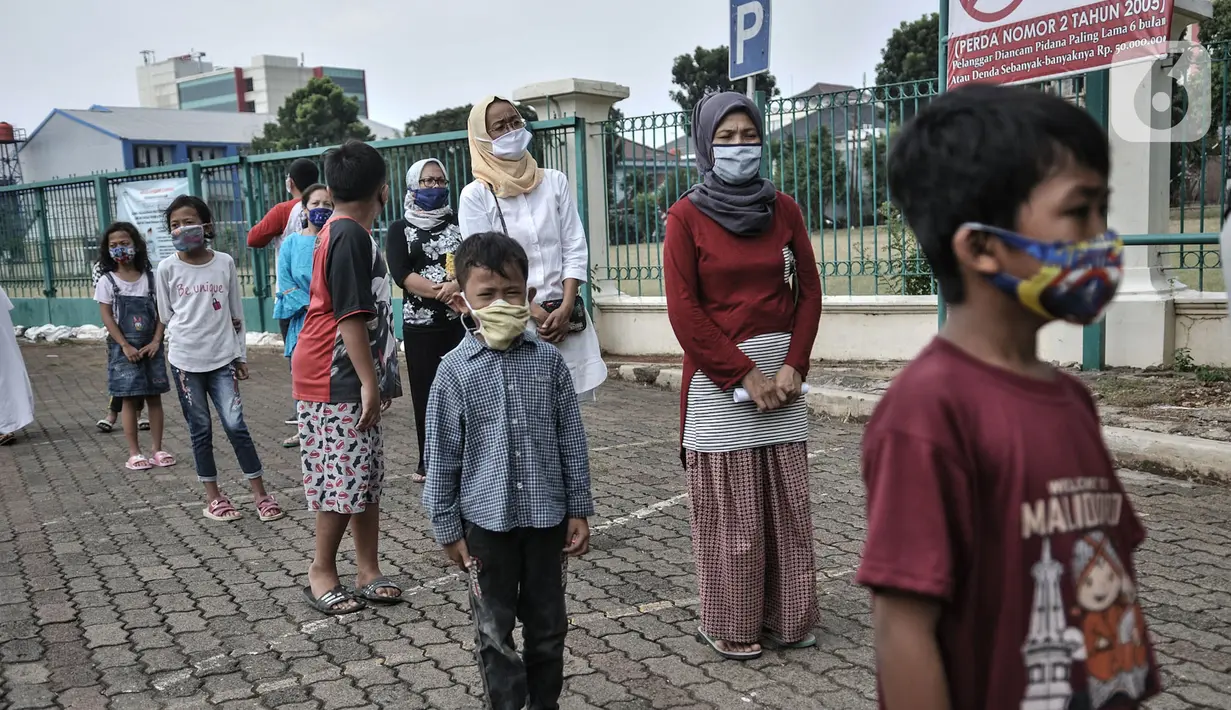 Anak-anak didampingi orang tua berbaris dengan standar protokol kesehatan saat antre menerima donasi ponsel yang diberikan Komunitas #WartawanLintasMedia saat acara #PonselPintarUntukPelajar di Jakarta, Minggu (9/8/2020). (merdeka.com/Iqbal S. Nugroho)