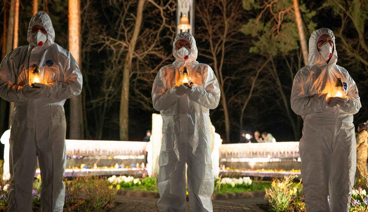 Orang-orang yang mengenakan pakaian pelindung putih memegang lilin selama upacara peringatan yang didedikasikan untuk petugas pemadam kebakaran dan pekerja yang meninggal setelah bencana nuklir Chernobyl, menjelang peringatan 40 tahunnya di Slavutych, Ukraina, Sabtu, 25 April 2026. (AP Photo/Dan Bashakov)