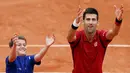 Petenis Serbia, Novak Djokovic, merayakan kemenangannya atas petenis Spanyol, Roberto Bautista Agut, bersama seorang ball boy dalam turamen tenis Prancis Terbuka 2016 di Roland Garros, Paris, (1/6/2016). (Reuters/Pascal Rossignol)