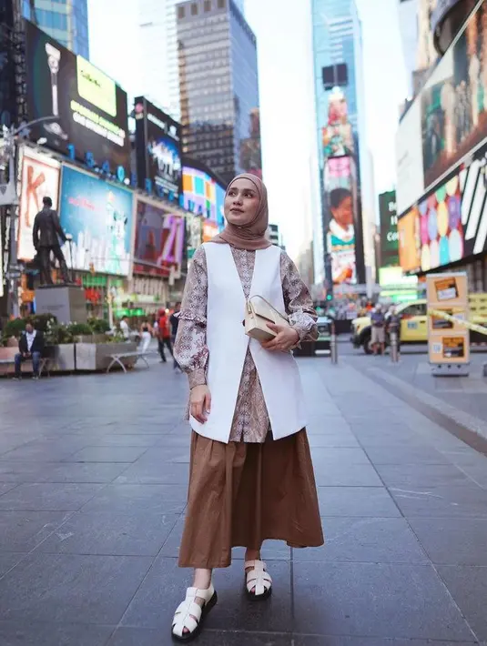Bergaya ala cewek bumi saat berpose di Time Square, Dwi tampil chic memadukan tunik penuh motif nuansa warna coklat, dipadukan dengan sleeveless outer putih dan rok coklat, serta hijab warna mocca. Ia juga melengkapi penampilannya dengan sepatu sandal putih dan tas kecil warna senada. (Instagram/dwihandaanda).