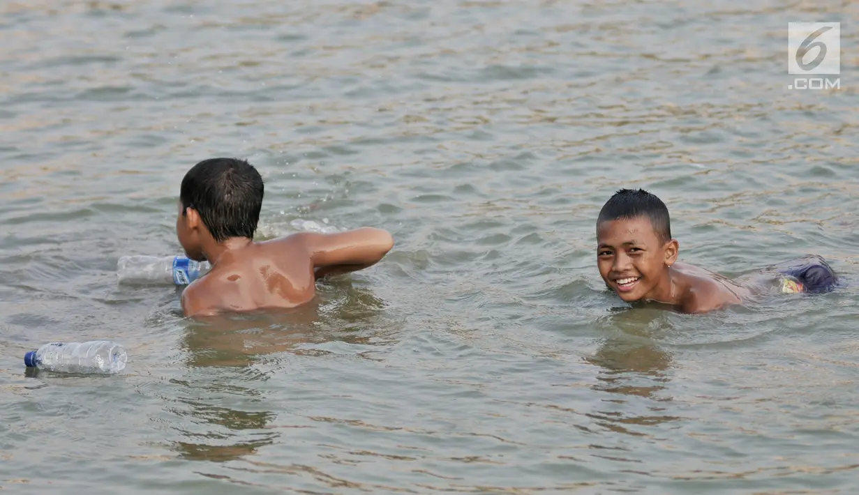 Anak-anak tertawa saat berenang di Danau Sunter, Jakarta, Selasa (23/7/2019). Anak-anak tetap nekat berenang di Danau Sunter kendati mereka sadar telah dilarang dan dapat membahayakan diri sendiri. (merdeka.com/Iqbal Nugroho)
