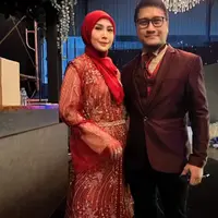 Fenita Arie hadir mengenakan setelan warna merah, dari atasan model baju kurung berbodir, celana panjag, hingga kerudungnya. Arie Untung juga mengenakan setelan jas maroon. [@ariekuntung]