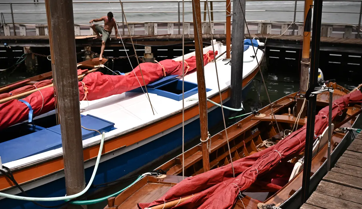 Seorang pria melompat di atas perahu sebelum acara Regatta Merah di Venesia, Italia, Minggu (20/6/2021). Acara ini bertujuan untuk merayakan tradisi bahari Venesia kuno dan untuk meningkatkan kesadaran tentang keseimbangan antara kota dan laut. (MARCO BERTORELLO/AFP)