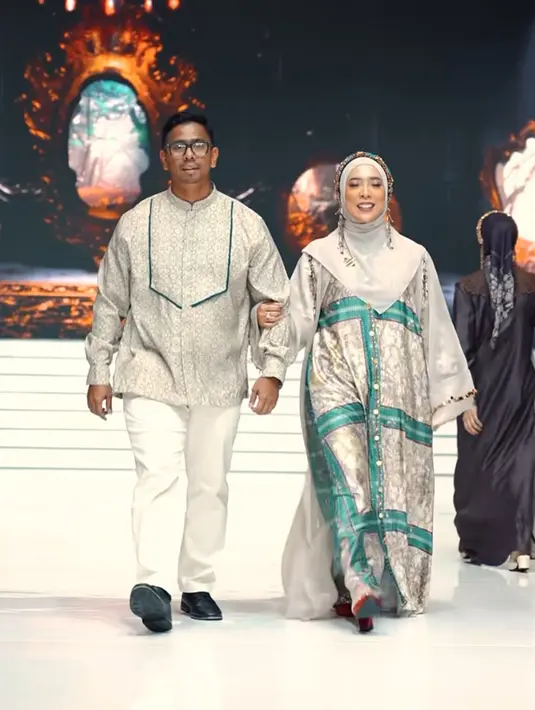 Fitri Tropica juga melenggang di runway koleksi Zaskia Sungkar bersama suaminya. Zaskia tampil dengan dress berkancing dengan warna abu-abu bercorak hijau dipadukan kerudung warna senada. Suaminya mengenakan baju koko lengan panjangnya. [@zaskiasungkar15]