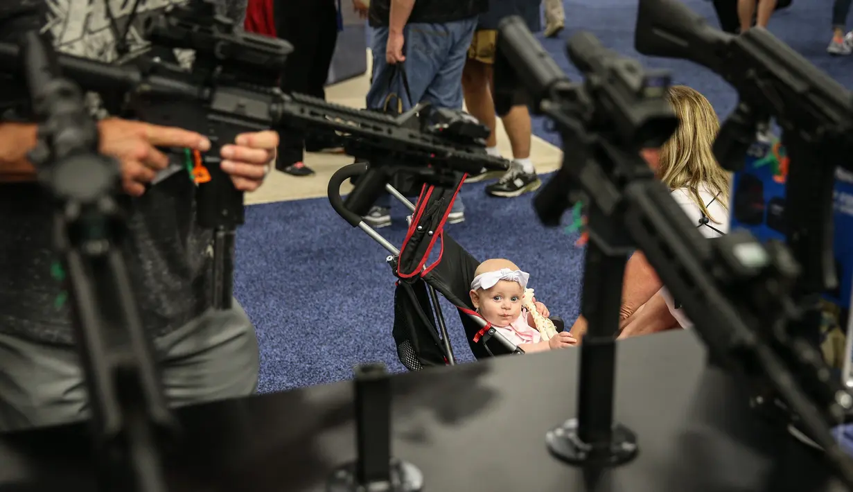 Seorang balita duduk di kursi dorongnya saat berada di pameran senjata di  konvensi tahunan NRA, Texas (6/5). Pameran ini menampilkan senjata canggih mulai dari yang ringan hingga kelas berat yang dipakai untuk militer. (AFP/Loren Elliot)