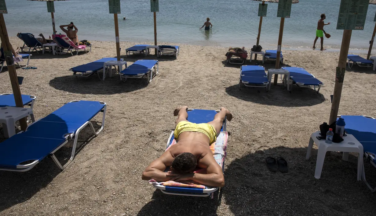 Seorang pria berjemur di pantai Desa Lagonissi, beberapa mil di barat daya Athena, Yunani, Kamis (29/7/2021). Suhu naik di atas 40 C (104 F) di beberapa bagian Yunani dan sebagian besar wilayah Eropa. (AP Photo/Yorgos Karahalis)