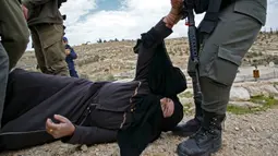 Polisi Israel membangunkan seorang perempuan Palestina yang terjatuh saat memprotes pembongkaran rumah di Desa Al-Dirat, dekat kota Hebron, Tepi Barat (16/1/2020). Pembongkaran itu menurut otoritas Israel dilakukan karena rumah dibangun tanpa izin. (AFP/Hazem Bader)