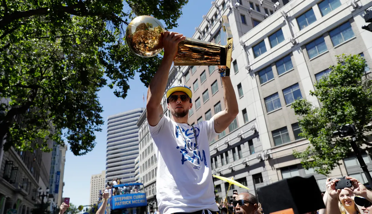 Pemain Guard Golden State Warriors, Stephen Curry menunjukkan tropi Larry O'Brien saat menggelar parade Warriors 2018 usai menjuarai NBA 2018 di pusat kota Oakland, California, Amerika Serikat, (12/6). (AP Photo/Marcio Jose Sanchez)