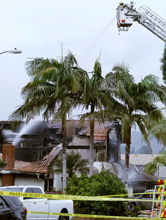 Petugas pemadam kebakaran menyemprotkan air di lokasi kecelakaan pesawat di sebuah rumah di Yorba Linda, California (3/2). Pesawat Cessna 414A jatuh di halaman belakang rumah warga di California, AS. (AP Photo/Alex Gallardo)
