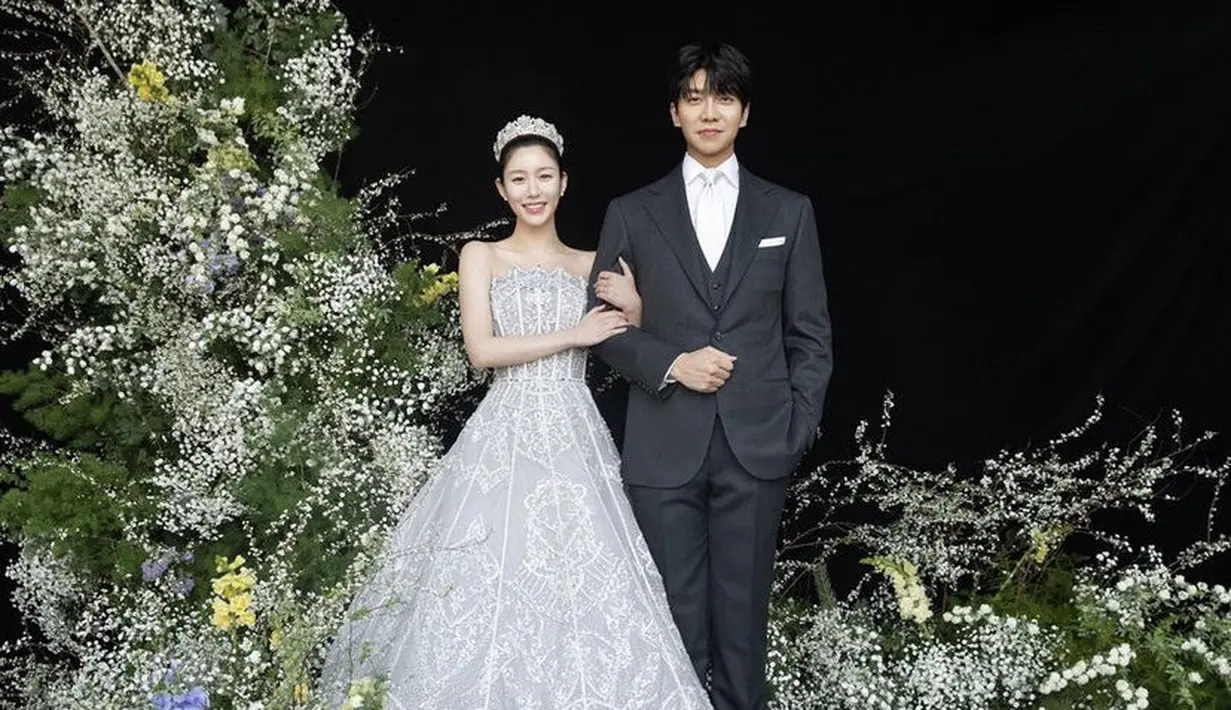 Dalam foto yang diambil di depan latar belakang dengan hiasan bunga yang megah, Lee Da In mengenakan gaun off shoulder putih yang indah sambil menggandeng tangan dengan suaminya. [Foto: IG/byhumanmade]