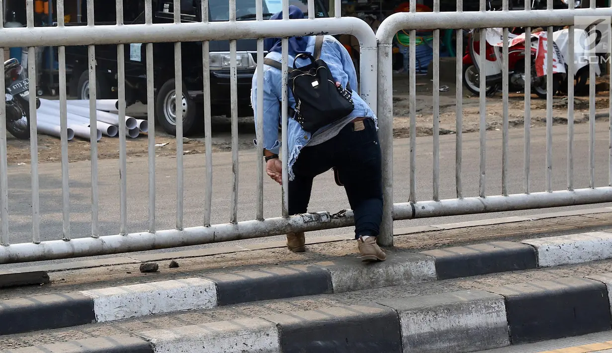 Seorang wanita menerobos pagar pembatas jalan di kawasan Pasar Minggu, Jakarta, Kamis (5/4). Kondisi Jembatan Penyeberangan Orang (JPO) yang tak kunjung diperbaiki membuat warga nekat menyeberang lewat celah pagar pembatas (Liputan6.com/Immanuel Antonius)