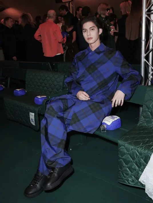Dalam acara tersebut, Bright tampil dibalut setelan warna biru dengan motif khas Burberry. Dari atasan model coat dan bawahan loosenya. Dipadukan sneakers hitamnya.  [@cloud9.ent.official]