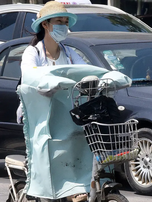 Seorang wanita mengenakan pakaian pelindung dari sinar matahari saat mengendarai sepeda listrik di Handan, provinsi Hebei, Rabu (12/7). Sebanyak 21 provinsi di China diterpa gelombang panas dengan suhu maksimum mencapai 50 derajat Celsius. (STR / AFP)