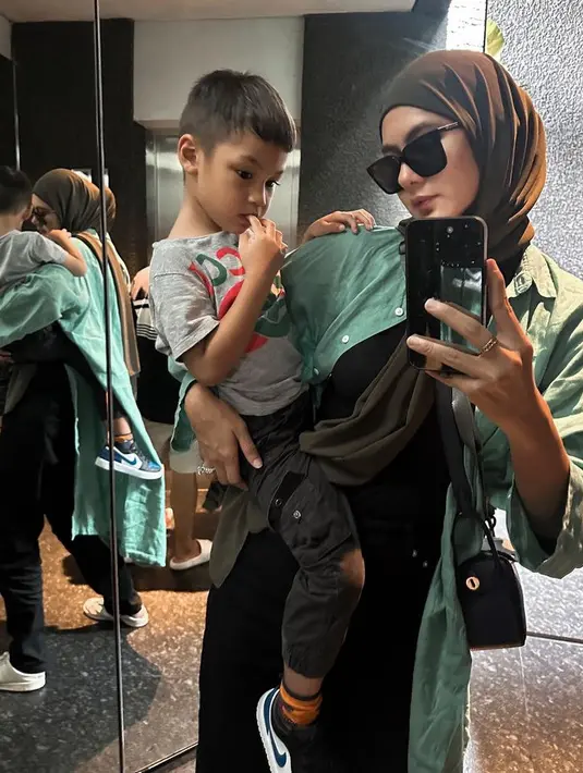 Paula tampil kasual mengenakan kerudung panjang hijau army dipadukan kemeja hijau lebih bright yang dikenakan sebagai outer. Ia pun mengenakan inner, celana, dan tas Hermes hitamnya. [@paula_verhoeven]