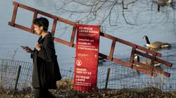 Pejalan kaki melewati stasiun tangga penyelamat es di pusat Central Park, wilayah Manhattan, New York, Senin (30/1/2023). New York City juga akan memecahkan rekor kedua, untuk periode waktu terlama tanpa salju. Pada Senin, sudah 327 hari tanpa akumulasi salju. Rekornya adalah 332 hari — rekor beruntun yang dipecahkan pada Desember 2020. (AP Photo/John Minchillo)