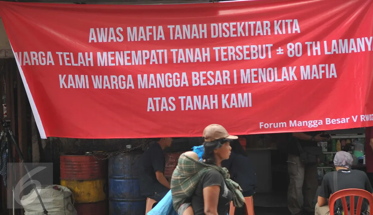 Seorang ibu menggendong anaknya berjalan di depan spanduk penolakan di kawasan jalan Mangga Besar, Jakarta, Senin (22/8). Spanduk itu dipasang warga RW2 Kelurahan Mangga Besar sebagai aksi menolak penggusuran rumah mereka. (Liputan6.com/Gempur M Surya)