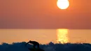 Seorang pria berselancar saat matahari terbenam di sebuah pantai di La Serena, Chile, Selasa (23/5/2015). (REUTERS/Marcos Brindicci)