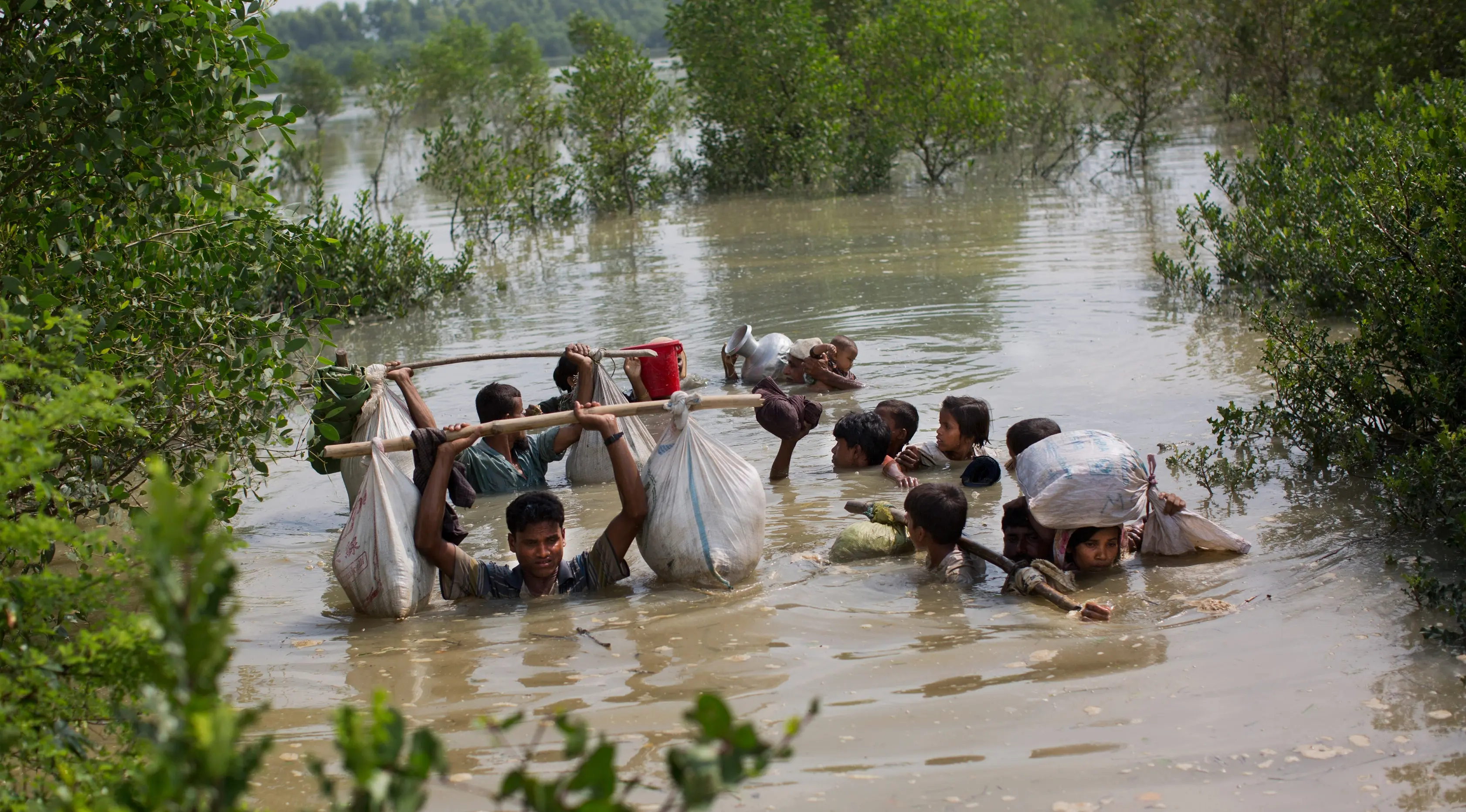 Sebuah keluarga dari etnis Rohingya membawa barang-barangnya melintasi sungai Naf untuk mencapai perbatasan Bangladesh di daerah Teknaf Cox's Bazar (5/9). (AP Photo/Bernat Armangue)
