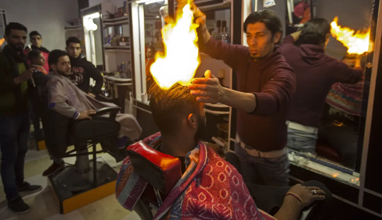Ramadan Edwan, seorang tukang cukur asal Palestina, menggunakan api untuk mencukur rambut pelanggannya di sebuah barbershop di kamp pengungsian Rafah, di selatan Jalur Gaza, Rabu (1/2). (MAHMUD HAMS/AFP)