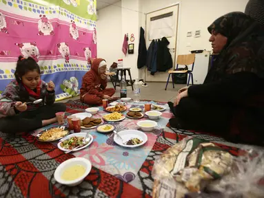 Seorang perempuan pengungsi yang tinggal bersama keluarganya di ruang kelas sekolah, setelah melarikan diri dari serangan udara Israel di pinggiran selatan Beirut, Lebanon, duduk untuk berbuka puasa bersama, pada 7 Maret 2026. Momen berbuka puasa Ramadan 1447 Hijriah di Beirut, Lebanon, berlangsung dalam situasi penuh keprihatinan. (Ibrahim AMRO/AFP)