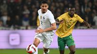 Bek Prancis William Saliba berebut bola dengan penyerang Afrika Selatan Bongokuhle Hlongwane dalam laga persahabatan di Stadion Pierre Mauroy, Rabu (30/3/2022) dinihari WIB. Timnas Prancis berpesta lima gol ke gawang Afrika Selatan. (DENIS CHARLET / AFP)